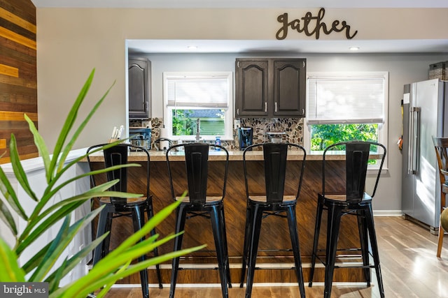 bar featuring dark brown cabinetry, sink, high end refrigerator, light hardwood / wood-style floors, and decorative backsplash