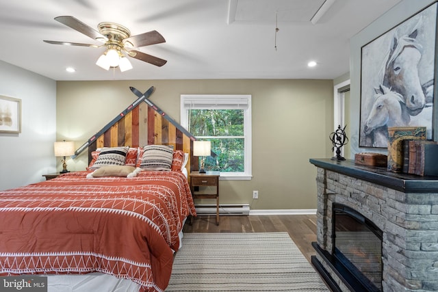 bedroom featuring ceiling fan, a stone fireplace, dark wood-type flooring, and baseboard heating