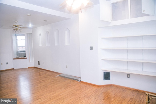 empty room featuring built in shelves, ceiling fan, and light hardwood / wood-style floors