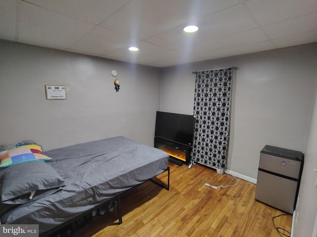 bedroom featuring a drop ceiling, light hardwood / wood-style floors, and stainless steel refrigerator