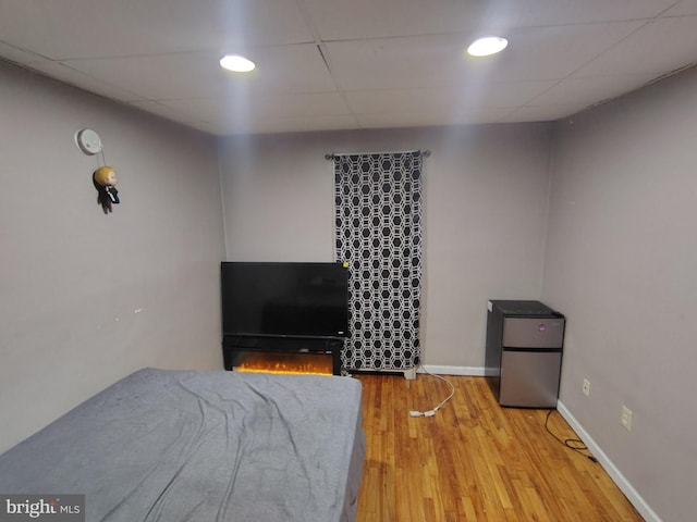 bedroom with a paneled ceiling, wood-type flooring, and stainless steel fridge