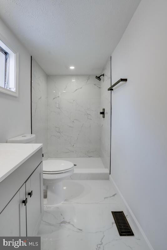 bathroom with vanity, toilet, a textured ceiling, and a tile shower