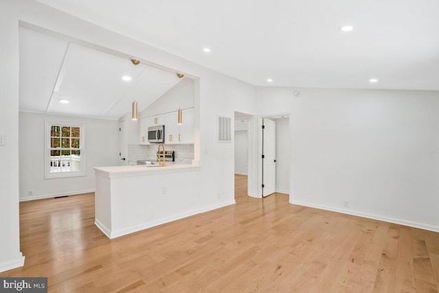 kitchen featuring lofted ceiling, appliances with stainless steel finishes, light hardwood / wood-style floors, white cabinets, and kitchen peninsula