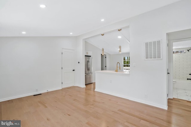 unfurnished living room with lofted ceiling, sink, and light hardwood / wood-style flooring