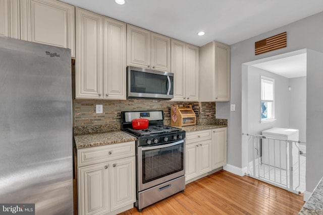 kitchen with decorative backsplash, appliances with stainless steel finishes, light stone counters, and light hardwood / wood-style flooring