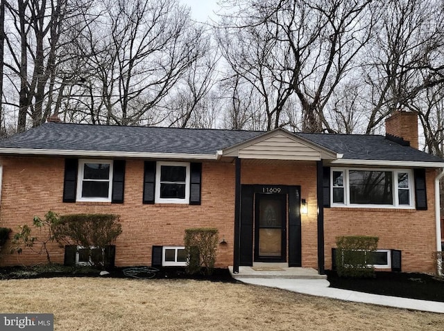 raised ranch featuring a front yard, a chimney, and brick siding