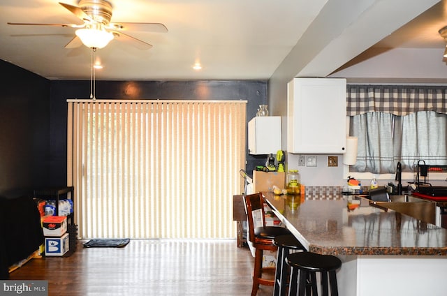 kitchen featuring white cabinetry, hardwood / wood-style flooring, ceiling fan, dark stone counters, and a breakfast bar area