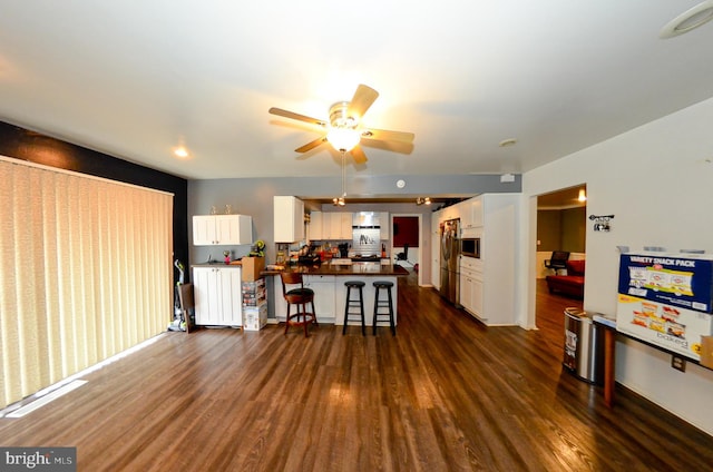 living room featuring kitchen peninsula, white cabinets, a kitchen bar, and dark hardwood / wood-style flooring