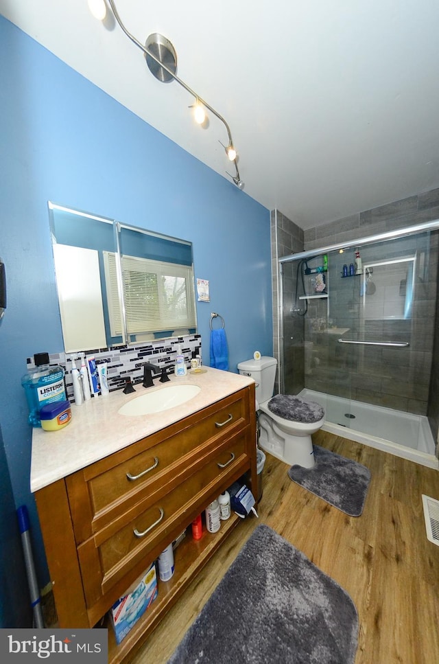 bathroom with toilet, wood-type flooring, vanity, walk in shower, and decorative backsplash