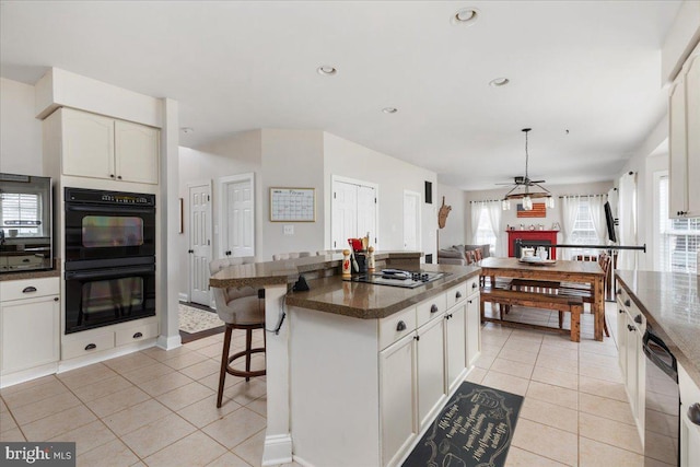 kitchen with gas stovetop, dark countertops, dobule oven black, white cabinetry, and a kitchen island