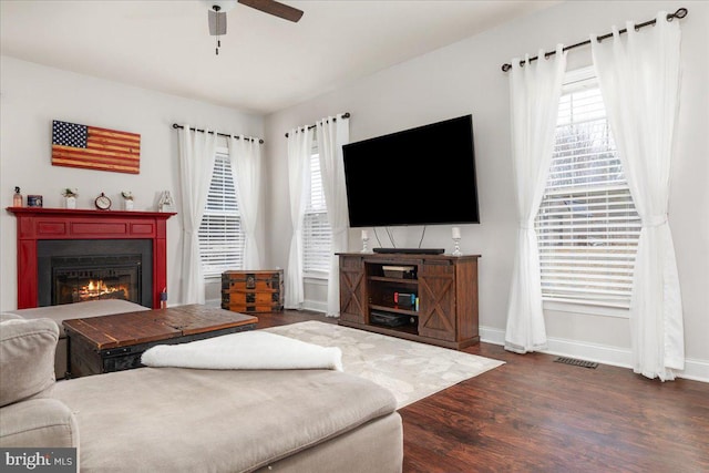 living room with a glass covered fireplace, dark wood-style flooring, ceiling fan, and baseboards