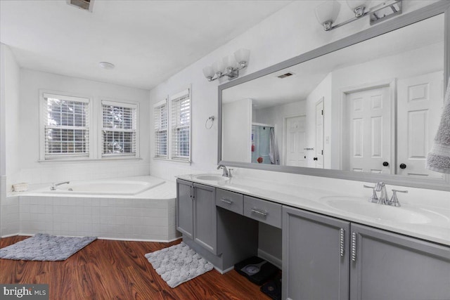 full bathroom featuring double vanity, a garden tub, a sink, and wood finished floors