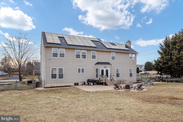 rear view of property featuring a fire pit, a patio, a chimney, and solar panels