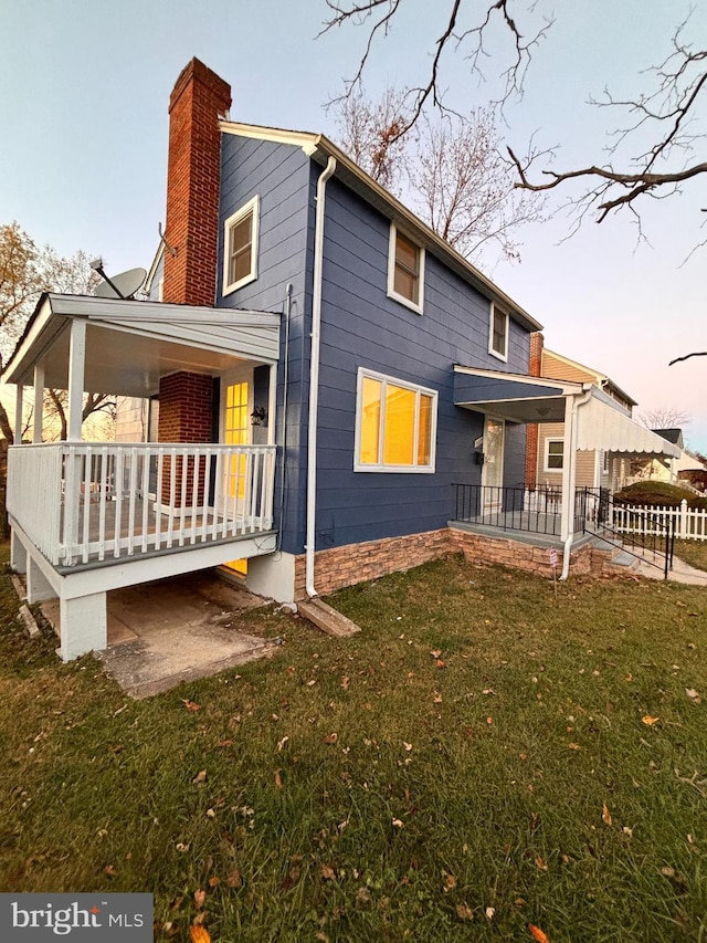 back house at dusk featuring a yard and covered porch