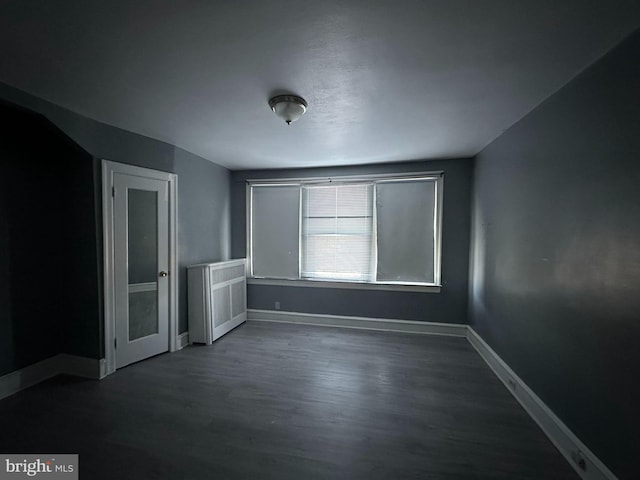 unfurnished room featuring radiator, baseboards, and dark wood finished floors