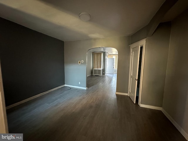 spare room with baseboards, arched walkways, and dark wood-style flooring