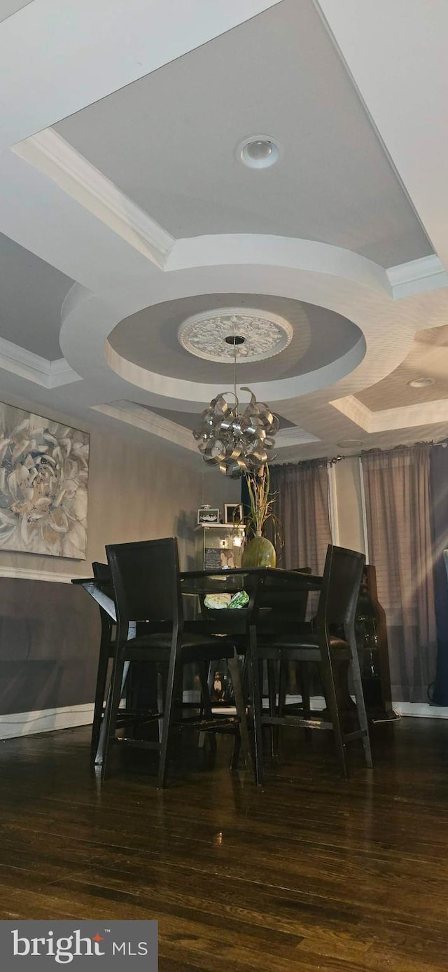 dining space featuring ornamental molding, dark hardwood / wood-style flooring, a raised ceiling, and a notable chandelier