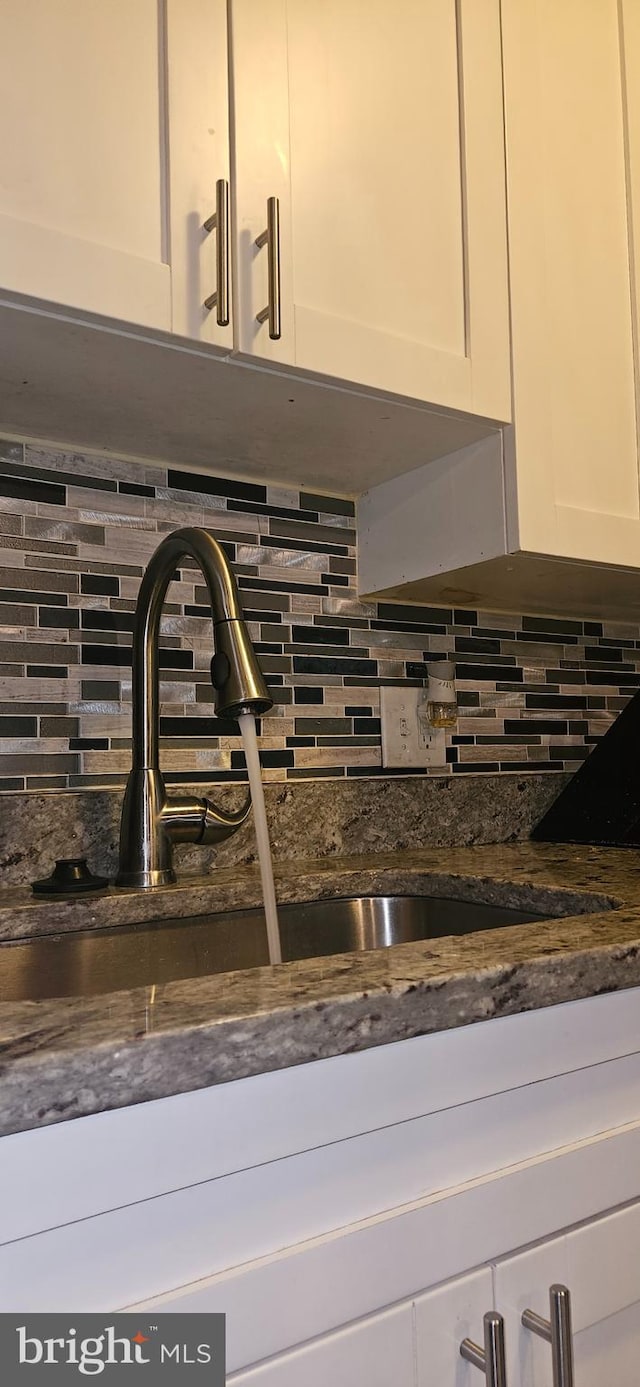 details featuring sink, decorative backsplash, dark stone counters, and white cabinets