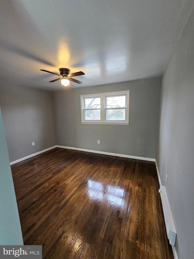 empty room with ceiling fan, a baseboard heating unit, and dark hardwood / wood-style floors