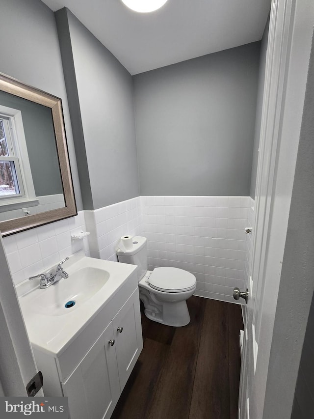 bathroom with wood-type flooring, toilet, vanity, and tile walls