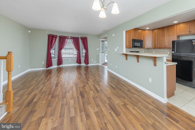 kitchen with a kitchen bar, decorative light fixtures, light wood-type flooring, decorative backsplash, and black appliances