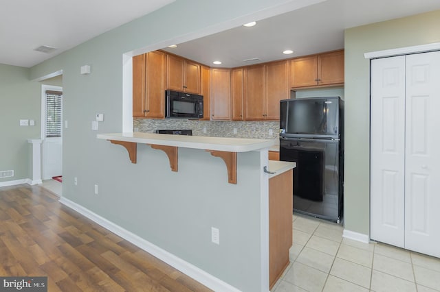 kitchen featuring light tile patterned floors, a breakfast bar area, tasteful backsplash, black appliances, and kitchen peninsula