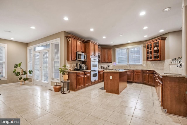 kitchen featuring light tile patterned floors, appliances with stainless steel finishes, tasteful backsplash, light stone countertops, and a kitchen island