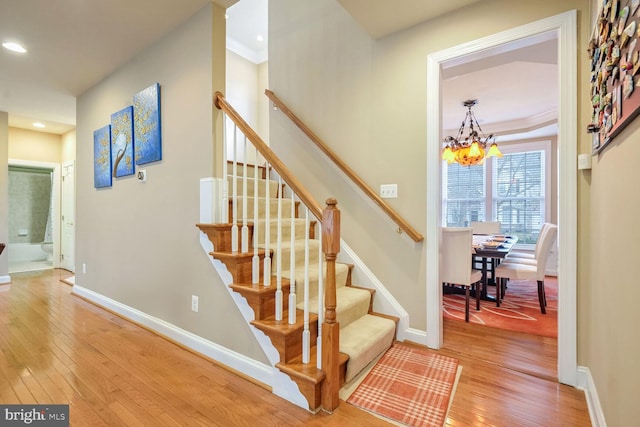 staircase featuring an inviting chandelier, hardwood / wood-style flooring, and crown molding