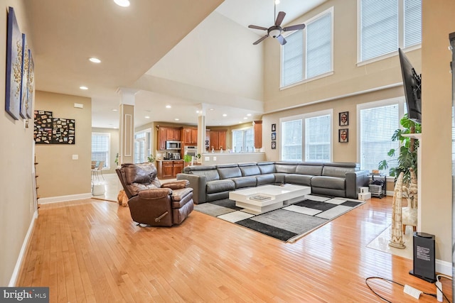 living room featuring ceiling fan, a towering ceiling, and light hardwood / wood-style flooring