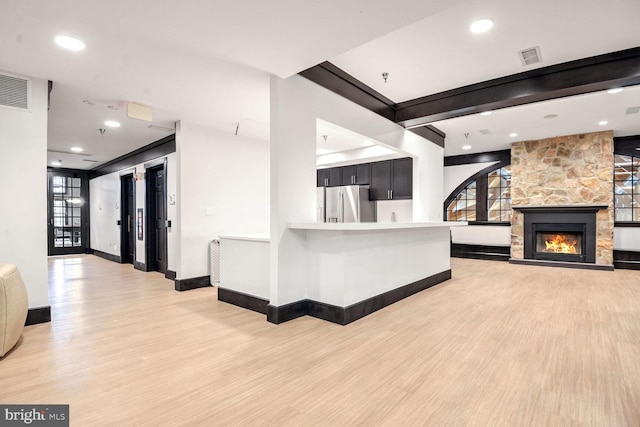 kitchen with a stone fireplace, stainless steel fridge, kitchen peninsula, beam ceiling, and light hardwood / wood-style flooring