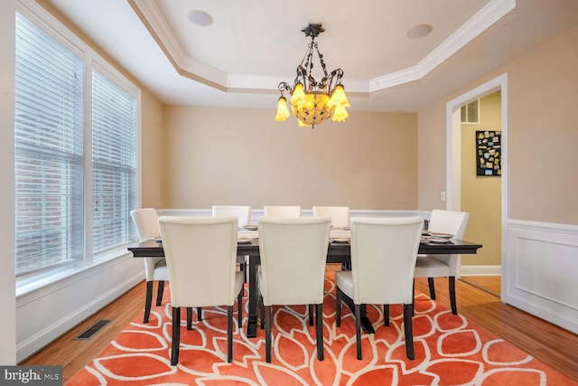 dining space with light hardwood / wood-style flooring, ornamental molding, a raised ceiling, and a chandelier