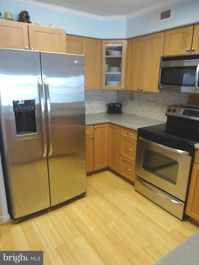 kitchen with crown molding, appliances with stainless steel finishes, decorative backsplash, and light hardwood / wood-style flooring