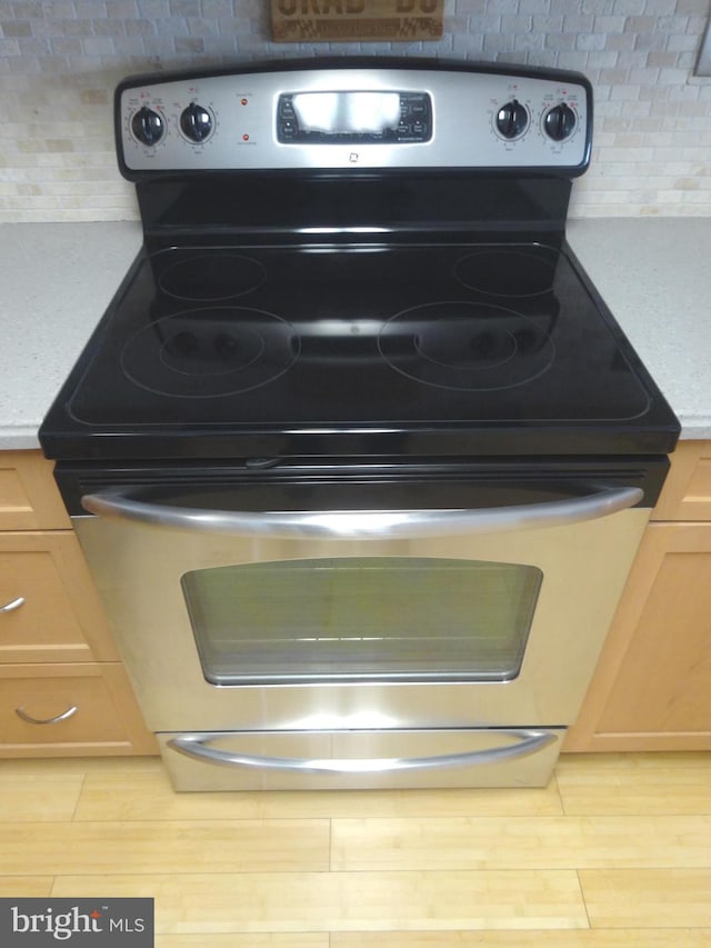 room details with stainless steel electric range oven, light brown cabinetry, light wood-type flooring, and backsplash