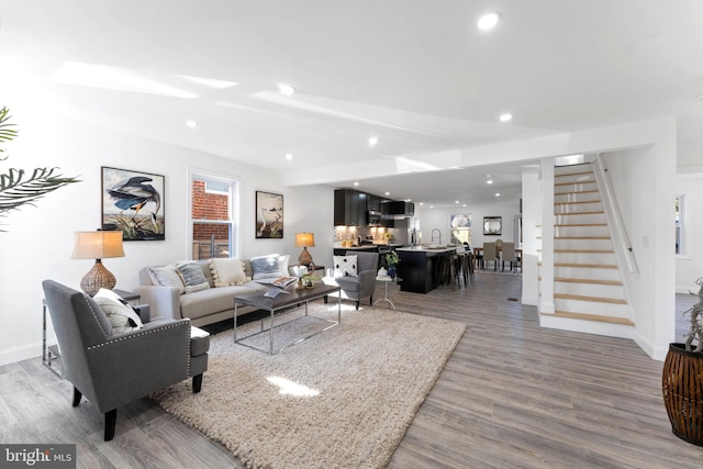 living room featuring stairs, baseboards, wood finished floors, and recessed lighting