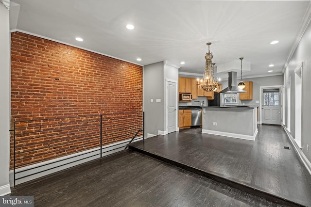 kitchen featuring dark countertops, brick wall, appliances with stainless steel finishes, island exhaust hood, and an inviting chandelier