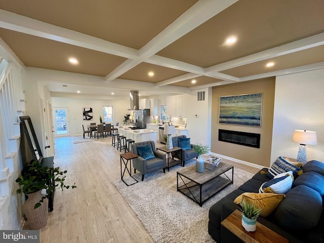 living area featuring recessed lighting, coffered ceiling, light wood-type flooring, beam ceiling, and a glass covered fireplace