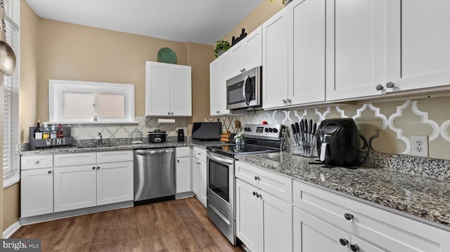 kitchen with white cabinetry, appliances with stainless steel finishes, dark hardwood / wood-style floors, and light stone counters