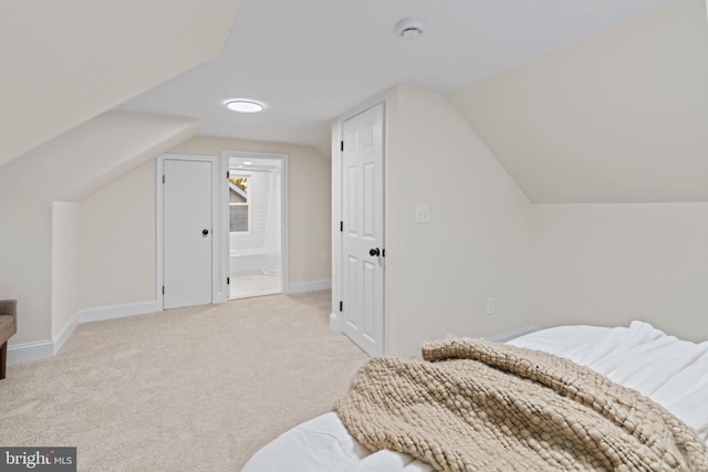 bedroom with vaulted ceiling, light carpet, and ensuite bathroom