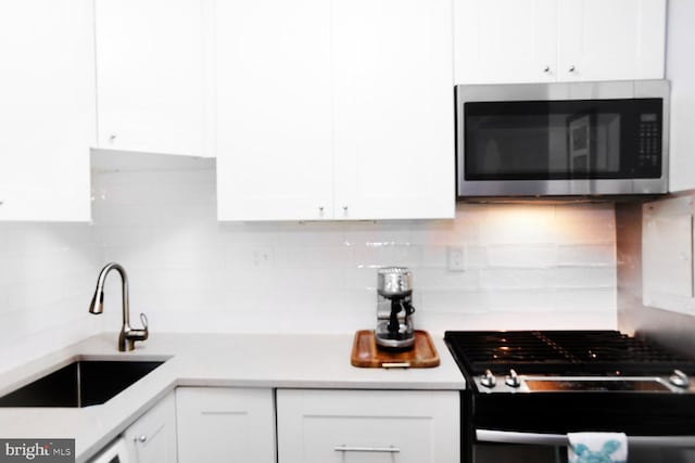 kitchen with sink, white cabinets, range with gas cooktop, and decorative backsplash