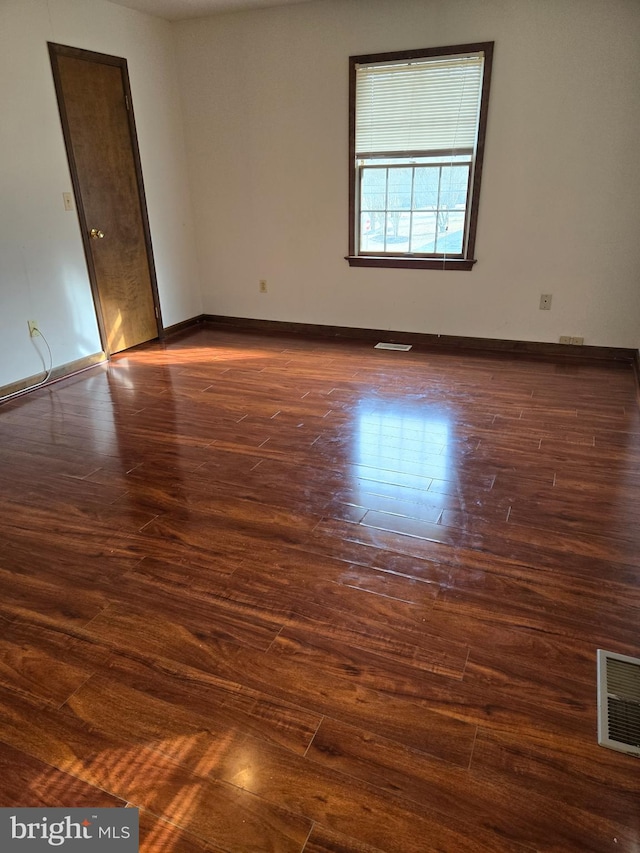 empty room with dark wood-style flooring, visible vents, and baseboards