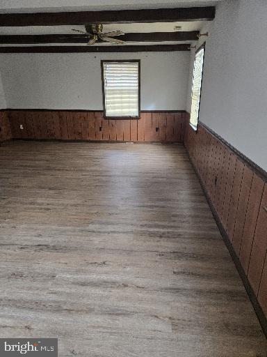 unfurnished room with wood walls, plenty of natural light, beamed ceiling, and wainscoting