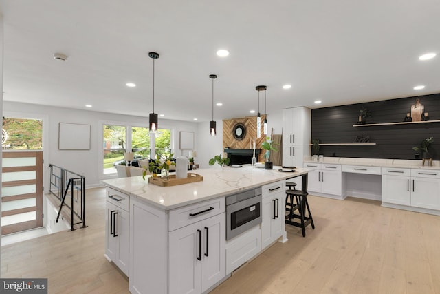 kitchen featuring white cabinetry, a kitchen island, stainless steel microwave, and decorative light fixtures