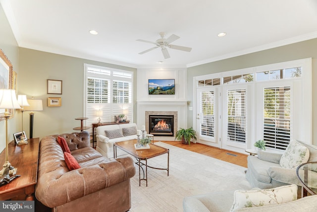 living room with crown molding, a glass covered fireplace, wood finished floors, recessed lighting, and a ceiling fan