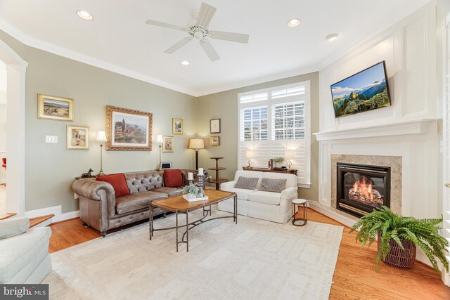 living room with crown molding, ceiling fan, wood finished floors, and a premium fireplace