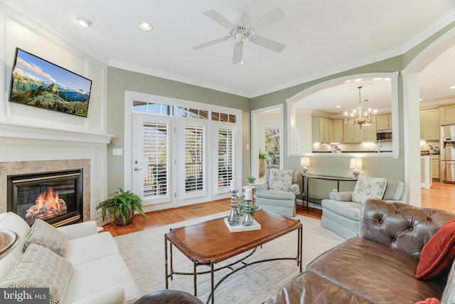 living area with arched walkways, ornamental molding, and light wood-type flooring