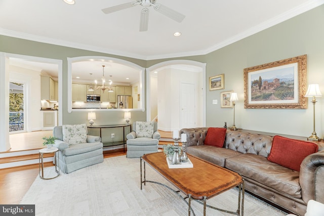 living area with arched walkways, ornamental molding, ceiling fan with notable chandelier, and light wood-style flooring