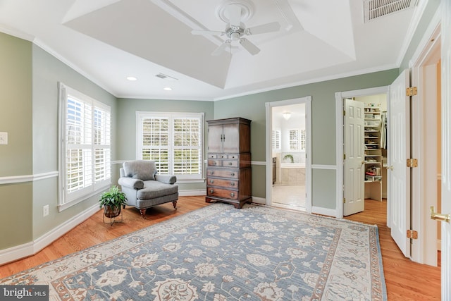 sitting room with ceiling fan, wood finished floors, a tray ceiling, visible vents, and ornamental molding