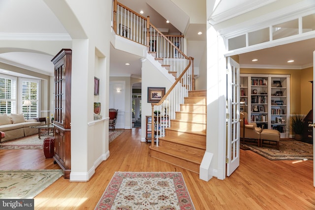 foyer entrance with arched walkways, french doors, stairs, light wood-type flooring, and ornamental molding
