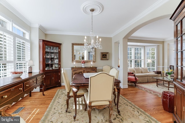 dining space with light wood-style floors, arched walkways, plenty of natural light, and an inviting chandelier