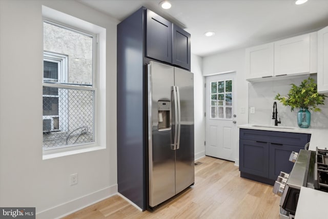 kitchen featuring white cabinetry, sink, stainless steel fridge, and light hardwood / wood-style floors